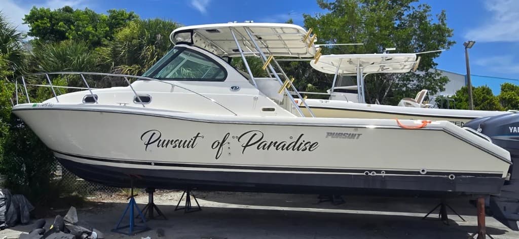 Pursuit of Paradise script lettering above a black boot stripe on a white Pursuit hull